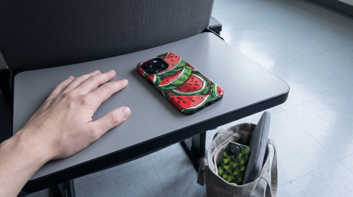 Green Camouflage iPhone tough case near the edge of a lecture desk with Watermelon in a tote on the floor below